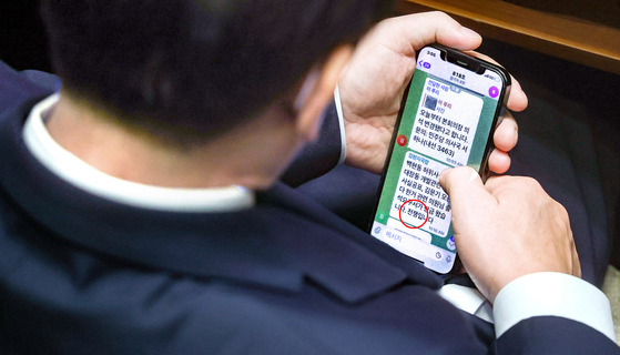 Democratic Party Chairman Lee Jae-myung reads a Telegram message sent by his aide during a plenary session of the National Assembly in Yeouido, western Seoul, Thursday, notifying him that prosecution has summoned him for questioning over allegations he spread false information about a 2015 land development scandal. The aide wrote, “This means war.” [JOINT PRESS CORPS]