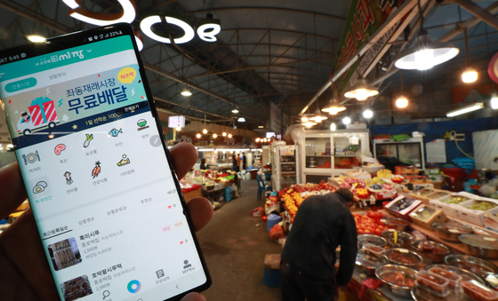 A shop owner at Jwadong Traditional Market holds up his phone to show a delivery service app. [YONHAP]