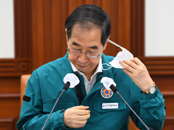 Prime Minister Han Duck-soo takes off his mask before speaking into the mic during the Covid-19 response meeting at the Government Complex in Seoul on Friday. Han announced in the meeting that the mandate on wearing masks during outdoor activities that involve more than 50 people in one setting will be lifted starting Monday. [NEWS1] 