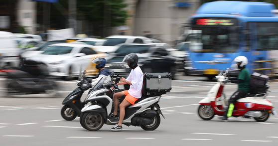 Delivery workers ride motorcycles in Seoul on June 28. [YONHAP]