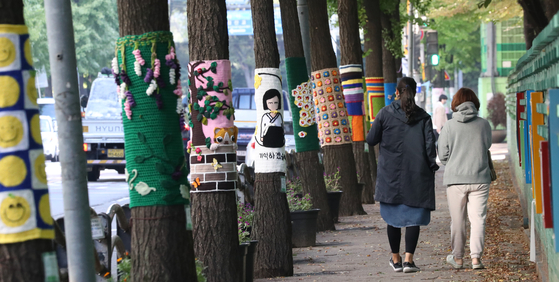 People pass by trees covered up with knitted clothes, a preparation for winter season, in Gwangmyeong, Gyeonggi, on Tuesday, as temperatures dropped rapidly. [NEWS1]