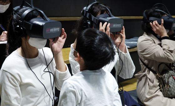 A child looks at his mother as she tries out a virtual reality (VR) interview at a job expo for foreigners married to Koreans, held at the Seoul Citizens Hall in Jung District, central Seoul, on Wednesday. A total of 19 companies participated in the job fair and conducted one-on-one interviews to recruit workers on site. Information on job openings of around 30 companies was also provided to those who came to the job fair. [YONHAP]