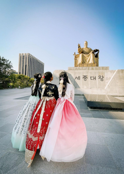 Visitors, dressed in traditional Korean hanbok, look up at King Sejong the Great at Gwanghwamun Square. [ALLAND DHARMAWAN]