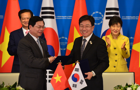 Trade ministers of Vietnam and Korea shake hands after signing the Vietnam-Korea free trade agreement on Dec. 10, 2014, in Busan. Korean President Park Geun-hye, right, and Vietnamese Prime Minister Nguyen Tan Dung, left, celebrate in the second row. [JOINT PRESS CORPS] 