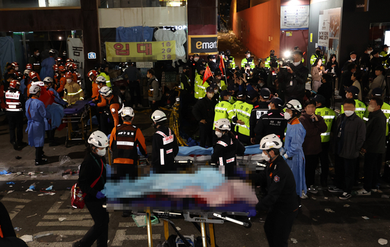 Emergency responders move bodies in Itaewon, Central Seoul, on Sunday. [YONHAP]