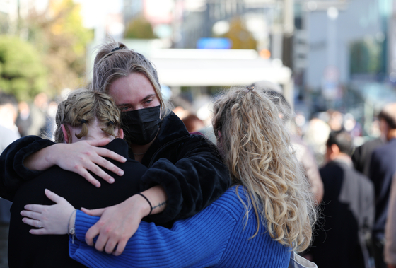Foreigners console each other after paying respects to the victims of the Halloween crowd crush at a makeshift memorial outside Exit No. 1 of Itaewon Station in Yongsan District, central Seoul, on Wednesday. [YONHAP]