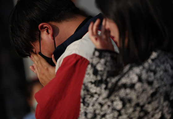 Mourners wipe away tears at one of the makeshift memorials for the victims of the Itaewon crowd crush located at Seoul Plaza, Jung District, central Seoul on Tuesday. [YONHAP]