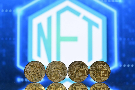 An illustration picture taken in London on December 30, 2021, shows gold plated souvenir cryptocurrency coins arranged by a screen displaying a NFT (Non-Fungible Token) logo. [AFP/YONHAP]