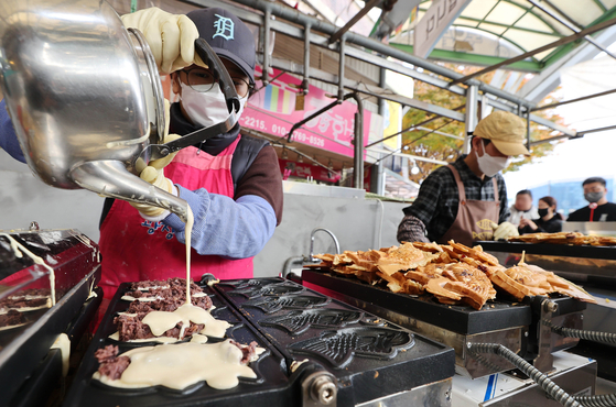A street vendor in Jongno District, central Seoul, on Thursday pours batter into an iron cast to make bbungeoppang, a fish-shaped winter snack usually with red bean or custard filling encased in a sweet batter and cooked until golden and crisp. The increase in orders of this pastry is a good indicator that winter is just around the corner. [YONHAP] 