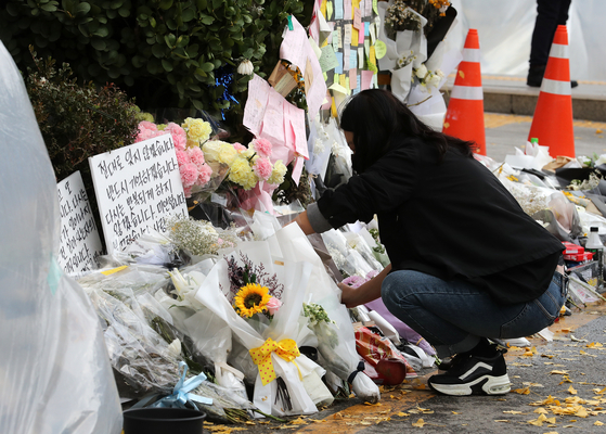 A volunteer reorganizes bouquets and letters at a makeshift memorial in front of Exit No.1 at Itaewon Station in Yongsan District, central Seoul, on Sunday. [NEWS1]