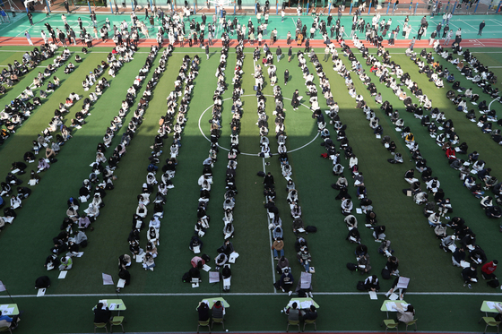 Students taking this year's College Scholastic Ability Test listen to instructions for the exam at Kyungpook National University High School in Daegu on Wednesday. The instructions were handed out outdoors to avoid the spread of the coronavirus. [YONHAP]