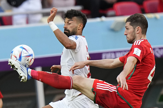 Iran's Ramin Rezaeian, left, and Wales' Ben Davies challenge for the ball during the World Cup group B soccer match between Wales and Iran, at the Ahmad Bin Ali Stadium in Al Rayyan, Qatar on Friday. Iran struck twice in the dying mintues of added time to earn a 2-0 victory over 10-man Wales. [AP/YONHAP]