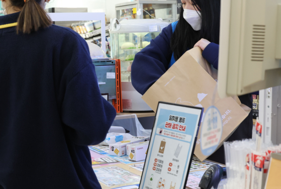 A convenience store cashier puts items into a paper bag on Thursday. [YONHAP]