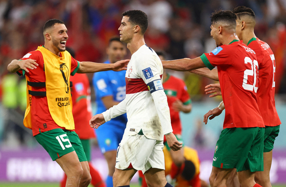 Portugal's Cristiano Ronaldo walks off the field after being eliminated from the World Cup as Morocco players celebrate winning the quarterfinal match 1-0. [REUTERS/YONHAP]