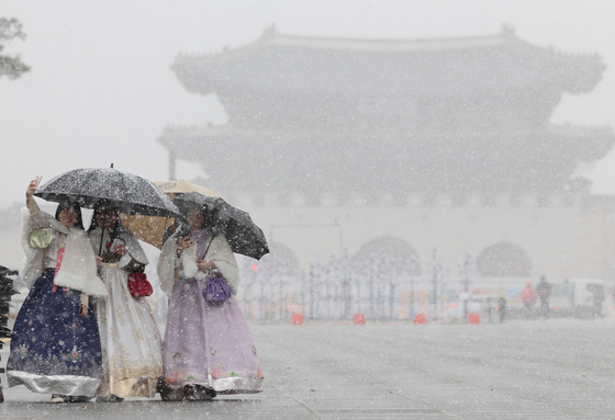 Tourists dressed in hanbok take a selfie with the Gyeongbok Palace in the background in Gwanghwamun, central Seoul, on Tuesday. While snow fell throughout the country, from Seoul to Gangwon and even in North Gyeongsang, levels of fine dust were very high. Temperatures are expected to drop on Wednesday. [YONHAP]