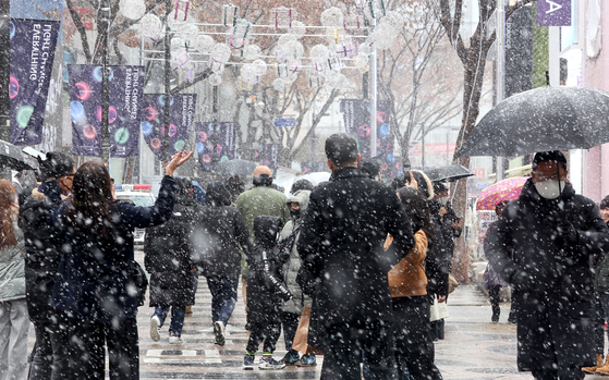 Seoul residents and tourists walk the streets of Myeong-dong in Jung District, central Seoul, on Tuesday afternoon as heavy snow falls in the Seoul Metropolitan area. [YONHAP]