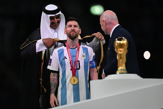 Qatari Emir Sheikh Tamim bin Hamad al-Thani, left, wraps a bisht around Argentinian forward Lionel Messi on stage next to the FIFA World Cup Trophy after Argentina won the 2022 Qatar World Cup final against France at Lusail Stadium in Doha on Dec. 18.  [AFP/YONHAP]