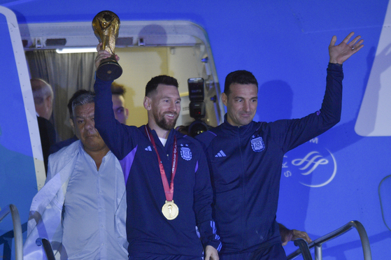 Lionel Messi holds the FIFA World Cup trophy as he deplanes, with coach Lionel Scaloni, in Buenos Aires, Argentina on Tuesday. [AP/YONHAP]