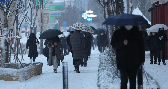 Passersby walk in the snow on Wednesday morning in downtown Seoul. Weather officials are warning of sinking temperatures from Thursday. [YONHAP]