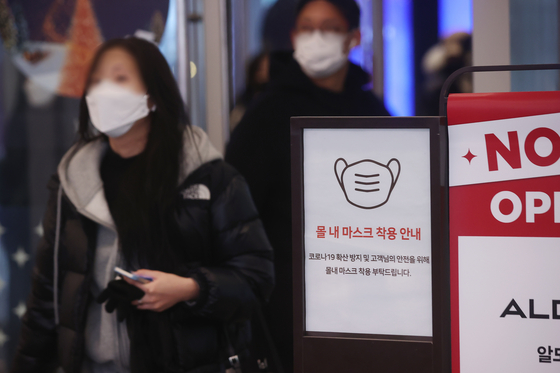 Visitors to a mall in Seoul walk past a sign on Thursday that reminds the public to wear their masks. [YONHAP]
