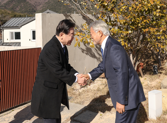 Lee Jae-myung, left, chairman of the Democratic Party (DP), shakes hands with former President Moon Jae-in at his home in Pyeongsan Village in Yangsan, South Gyeongsang, Monday. [DEMOCRATIC PARTY]