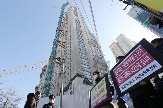  A group of people asking for compensation from HDC Hyundai Development after the collapse of an apartment building in Gwangju stand in front of the site of the collapse on Tuesday. Wednesday is the first anniversary of the collapse, which killed six workers. [YONHAP] 