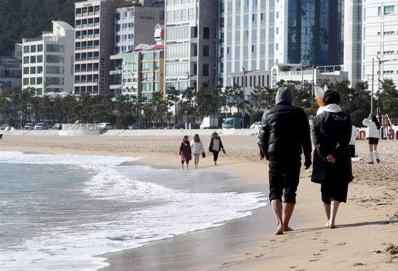 People walk along Haenudae Beach in Busan on Wednesday with their pants rolled up and dressed in lighter winter coats as the weather has become unseasonably mild. According to the Korea Meteorological Administration on Wednesday, temperatures will be 5 to 10 degrees Celsius higher than in previous years through Friday. [YONHAP]
