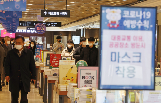 Shoppers in a book store in Seoul walk down an aisle with a sign that reminds the public to wear their masks. [YONHAP]