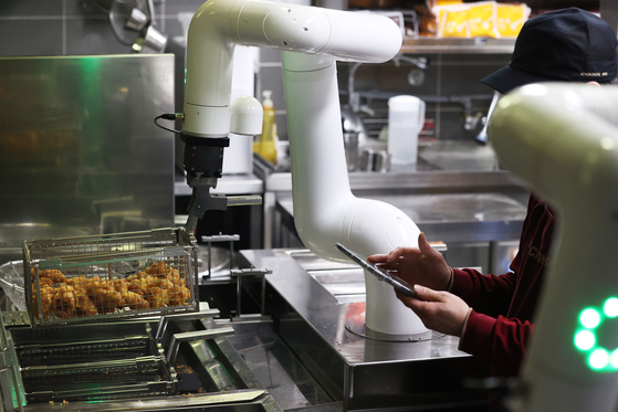 On Wednesday, an employee observes a chicken-frying robot during the cooking process at Kyochon, a fried chicken restaurant, in Namyangju, Gyeonggi. Kyochon F&B said it began operating the robots at three branches starting on Wednesday. [YONHAP]
