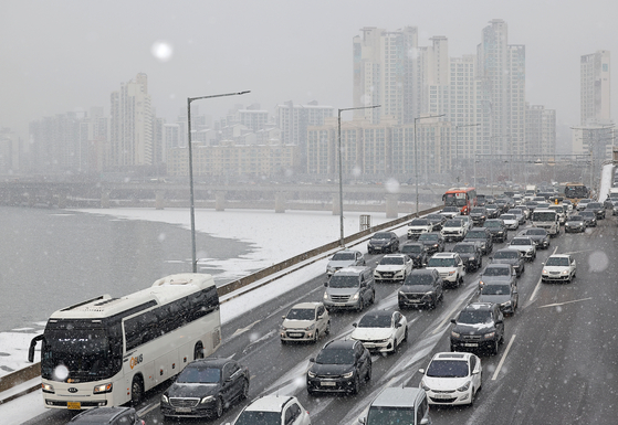 Cars drive slowly on a road in Seoul on Thursday morning due to heavy snow. [YONHAP]