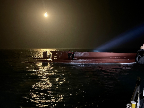 Coast Guard officials stand on the overturned keel of a capsized fishing vessel approximately 16.6 kilometers west of Daebichi-do, an island off the coast of Mokpo, South Jeolla, in the early hours of Sunday. [YONHAP]