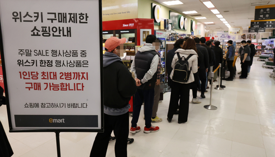 Buyers line up at Emart's Yongsan branch in central Seoul on Jan. 6 to buy whisky after Emart announced it would be discounting seven popular whisky brands. A sign reads that sales of whisky are limited to two bottles per customer. [YONHAP]