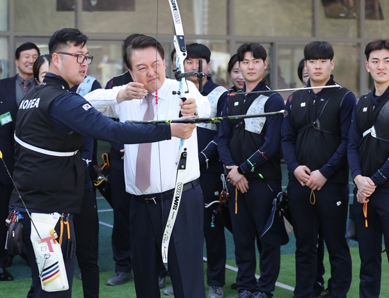 President Yoon Suk Yeol, center, fires an arrow with the help of two-time Olympic gold medalist and three-time world champion archer Kim Woo-jin at the Jincheon National Training Center in Jincheon, North Chungcheong on Tuesday. Yoon toured the training center after discussions on the 2023 Korea Sports Vision Report.  [YONHAP]