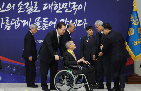 President Yoon Suk Yeol, second from left, pushes the wheelchair of Son Jae-han, who was conferred a state award at the Yongsan presidential office in Yongsan District on Thursday for donating more than 70 billion won ($54 million) to establish a scholarship program and sponsoring scholarships to students for the past decade. A total of 19 people — including Son, who was awarded the Peony Medal of the Order of Civil Merit — received state awards on Thursday. [YONHAP] 