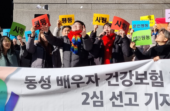 So Sung-wook and Kim Yong-min celebrate the ruling of the Seoul High Court on Tuesday that recognized So as a legal dependent of Kim in a health insurance scheme. The couple and civic groups held a press conference in front of the court in Seocho District, southern Seoul, on Tuesday. [YONHAP]
