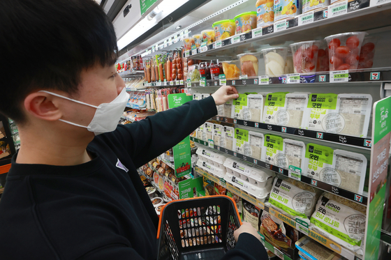 A customer selects a tofu product from the low-priced food section at a 7-eleven convenience store in Seoul amid rising consumer prices and higher interest rates on Feb. 5. [YONHAP]
