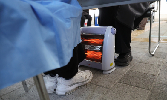 The medical staff at a Covid-19 testing center in Mapo District, western Seoul, warm their feet by an electric heater on Monday morning. [YONHAP]