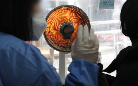 An electric heater warms the medical staff at a Covid-19 testing center in Mapo District, western Seoul, on Monday. [YONHAP]
