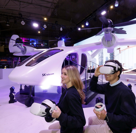 Models try on a virtual reality headset for an air taxi ride simulation in front of a life-size mock-up of an urban mobility vehicle (UAM) built by Joby Aviation, at a UAM experience zone set up by SK Telecom at the MWC 2023 event. The MWC, or Mobile World Congress, will run for four days starting Monday in Barcelona, Spain. [JOINT PRESS CORP]