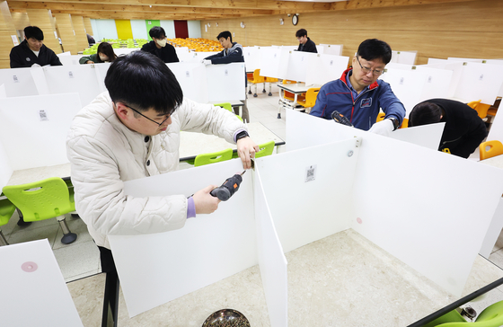 Teaching staffers at Samil Technical High School in Suwon, Gyeonggi, remove partitions that divide tables at the school's cafeteria on Monday, installed as a safety measure to prevent Covid-19, ahead of the new academic semester in March. Students will no longer be required to check their temperatures when arriving at school starting this semester. Korea's new Covid-19 cases hit the lowest figure in eight months on Monday, dropping to 4,026. The weekly average dropped by 15 percent every week over the past month, according to the Central Disaster and Safety Countermeasure Headquarters on Monday. [YONHAP] 