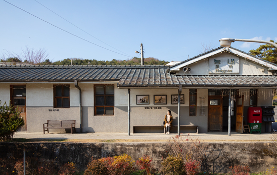 A woman sits outside of Neungnae Station. The wooden benches and the red mailbox outside the station are popular photo spots. [GYEONGGI TOURISM ORGANIZATION]