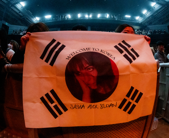 Fans hold up a Korean flag decorated with Sasha Alex Sloan's face during the singer's first concert in Korea held on Monday at the Yes24 Live Hall music venue in eastern Seoul as a part of her ″I Blame The World″ Asia tour. [LIVE NATION KOREA]