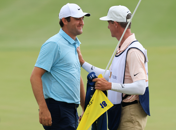 Scottie Scheffler celebrates with caddie Ted Scott after winning on the 18th green during the final round of The Players Championship on The Players Stadium Course at TPC Sawgrass on Sunday in Ponte Vedra Beach, Florida. [GETTY IMAGES] 