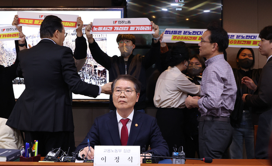 Members of the Korean Confederation of Trade Unions protest behind Labor Minister Lee Jung-sik during a discussion on the working hour reform plan with other labor representative held in Seoul on Wednesday. [YONHAP]