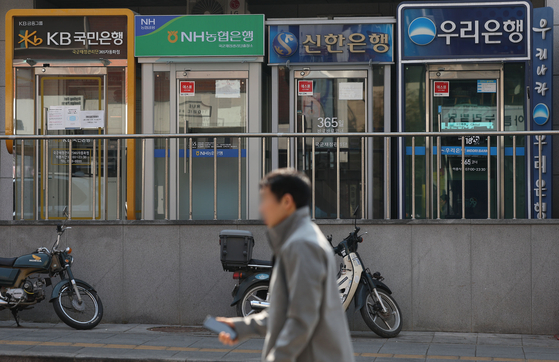 A passerby walks by ATMs in Sunday in central Seoul. The number of employees at Korea's five major commercial banks — KB Kookmin, Shinhan, Woori, Hana and NongHyup Bank — fell by more than 1,000 every year since 2018. There were a total of 69,751 employees of the five banks as of last year, down 4,444, or down 6 percent, compared to the end of 2018. [YONHAP]