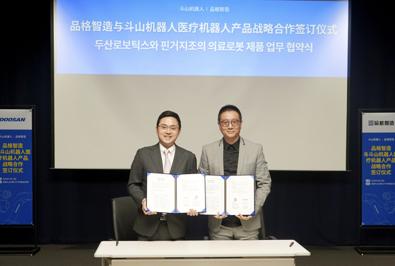 Doosan Robotics CEO Ryu Jung-hoon, left, takes a photo with Liang Zhihong, CEO of Guangxi Pinge Digital Industry Intelligent after signing an agreement to develop a medical robot. [DOOSAN ROBOTICS]