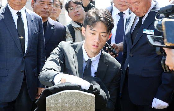 Chun Woo-won, grandson of the late military dictator and former President Chun Doo Hwan, wipes a gravestone belonging to a victim of the May 18 Gwangju Uprising with his coat on Friday at the May 18th National Cemetery in Gwangju. [YONHAP]