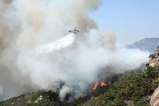 A helicopter puts out a fire that has broken out on Mount Inwang in Jongno District, central Seoul on Sunday. [YONHAP]