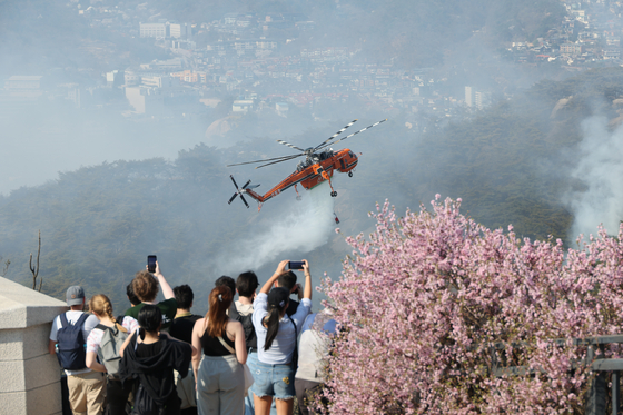 Hikers watch a helicopter put out a fire that broke out on Mount Inwang in Jongno District, central Seoul on Sunday. [YONHAP] 