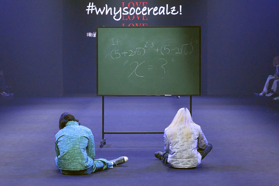 A scene from #whysocerealz!'s Seoul Fashion Week 2023 Fall/Winter show last month. Here shows two models sitting in front of a chalkboard that is covered with equations, appearing stumped. [#WHYSOCEREALZ!]